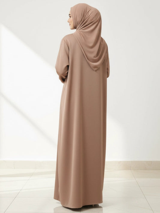 Woman wearing a long, light brown abaya in a minimalistic setting